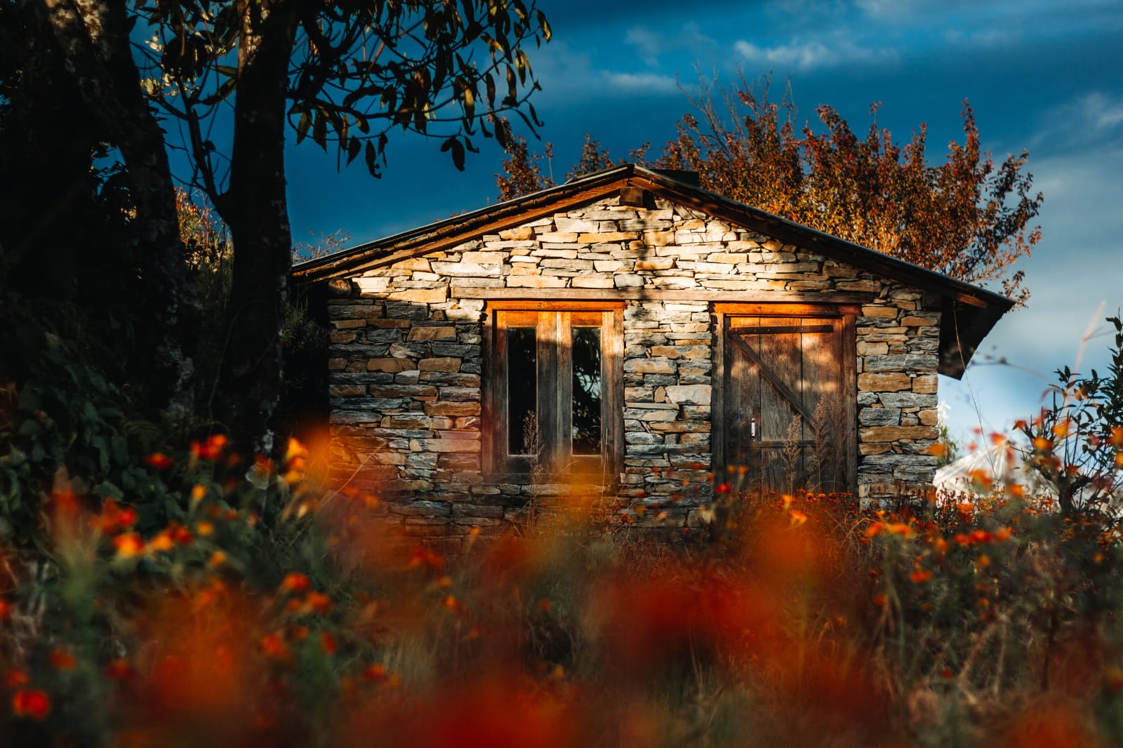 Stone cottage at Shama Basecamp surrounded by autumn flowers in the Kumaon Himalayas